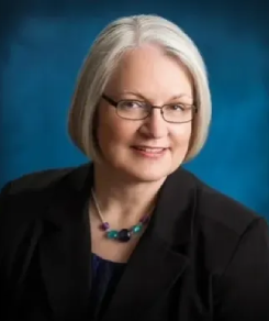 A woman with white hair wearing glasses and a black jacket.