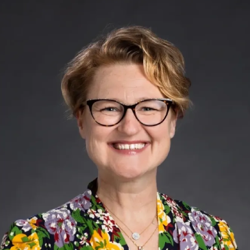 A woman with glasses and short hair wearing a floral shirt.