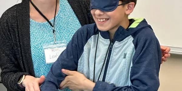 A boy participating in the Global Neuro Ycare Program is wearing a blindfold in a classroom.